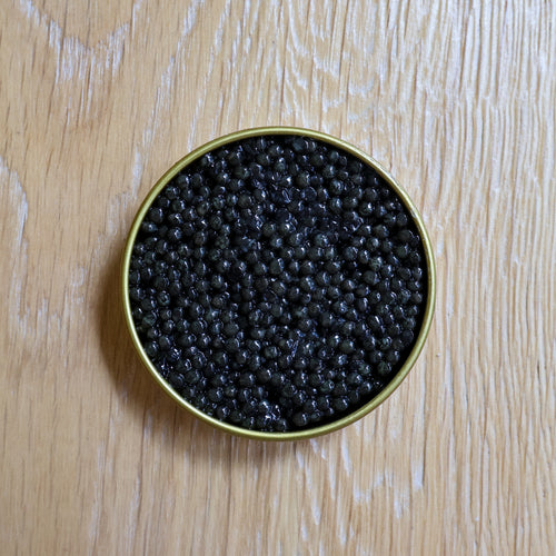 Gold tin filled with black caviar on a wooden surface