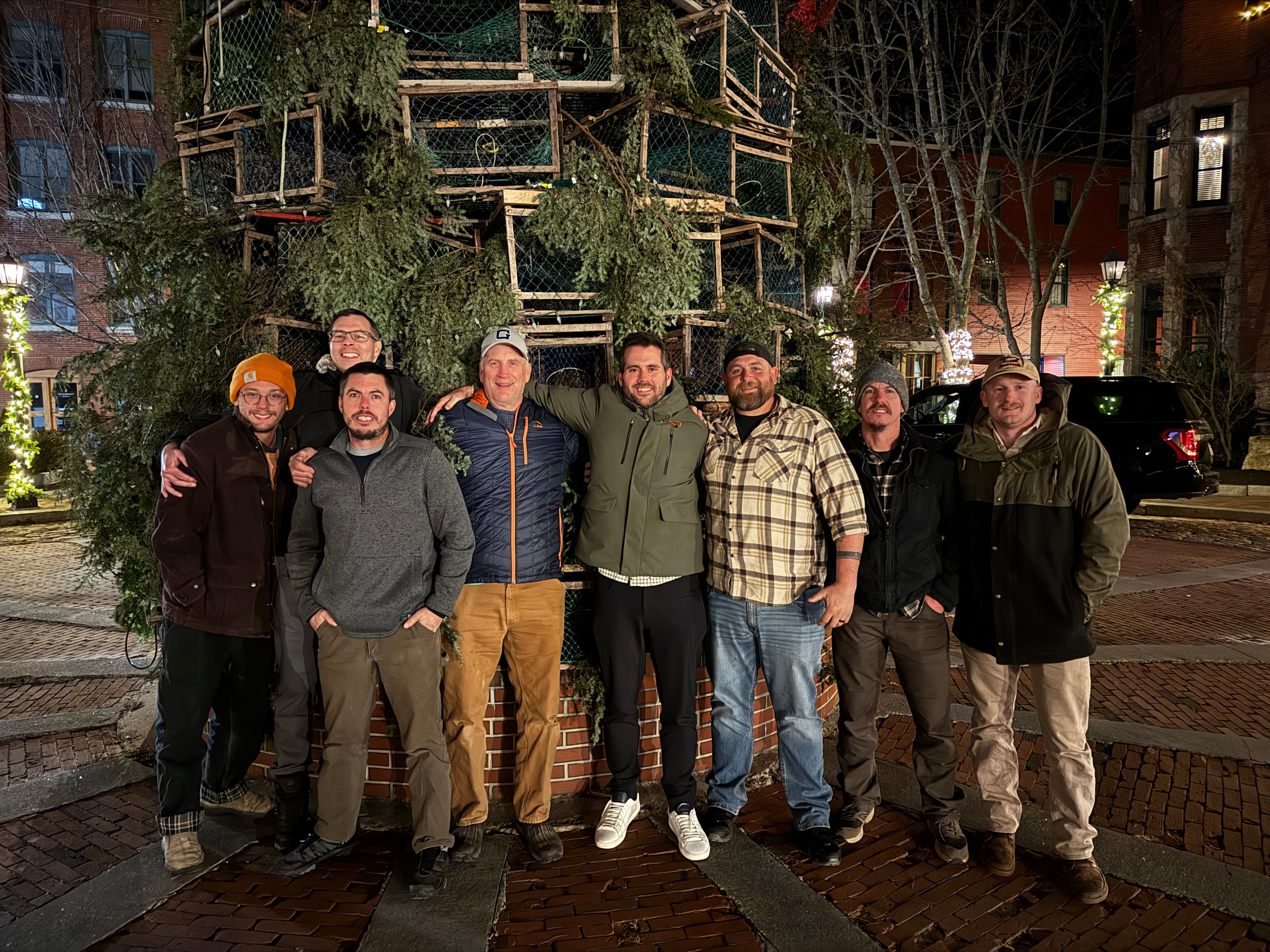 Group of people posing in front of a decorative Christmas tree on a city street at night.