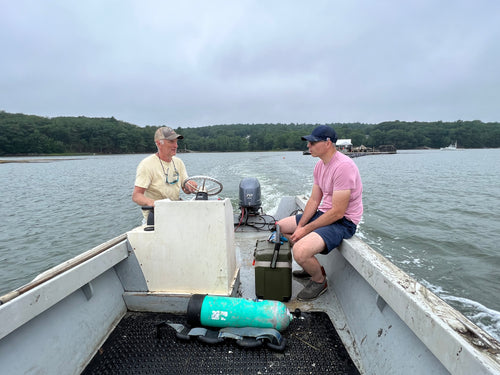 Two men on a boat with equipment on a body of water