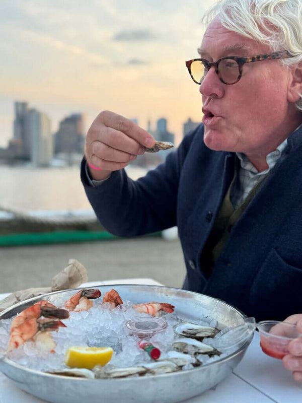 Man eating oysters on a boat with a city skyline in the background