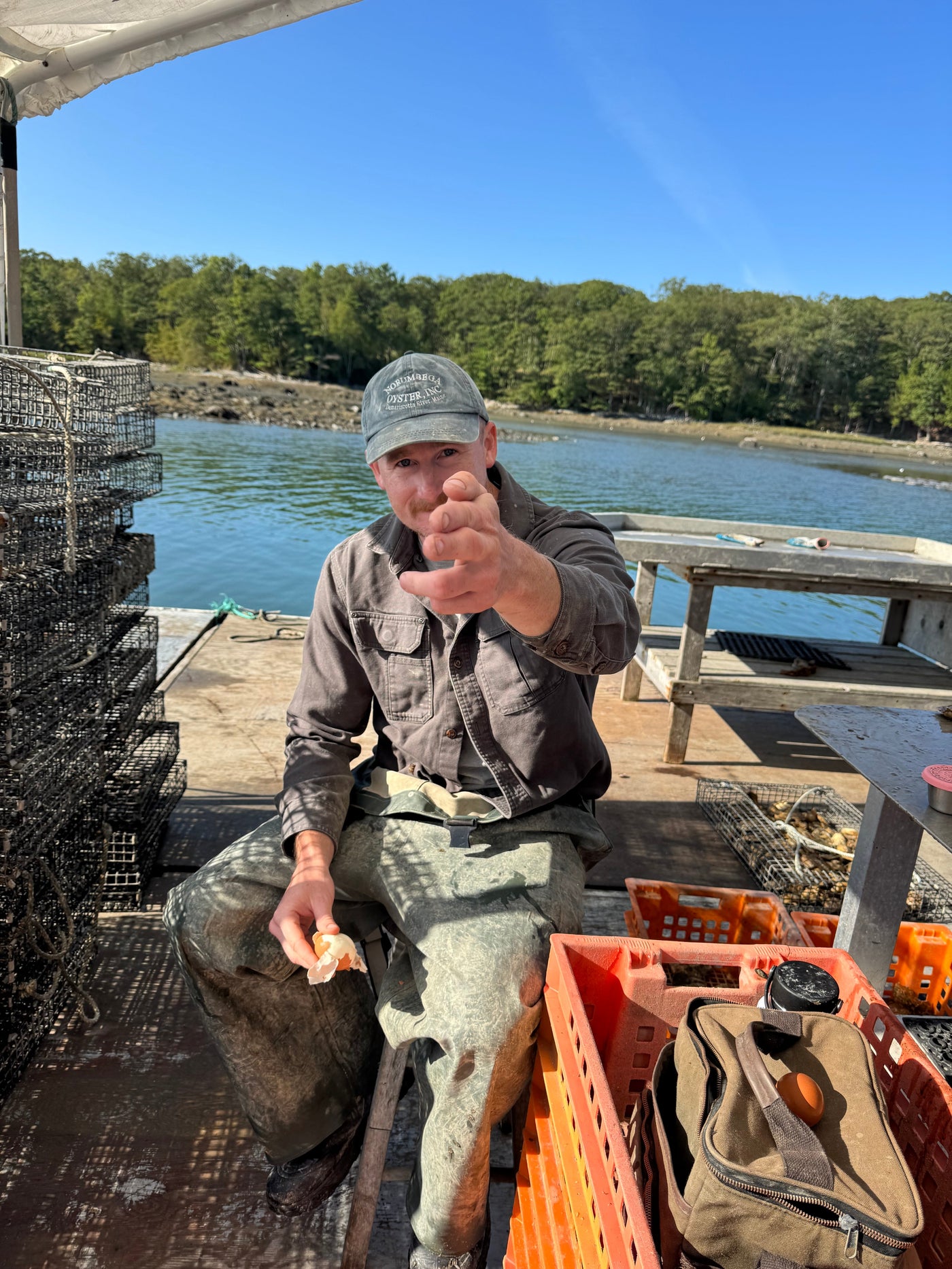 Norumbega oyster farmer on a dock by the Damariscotta River holding a fresh oyster